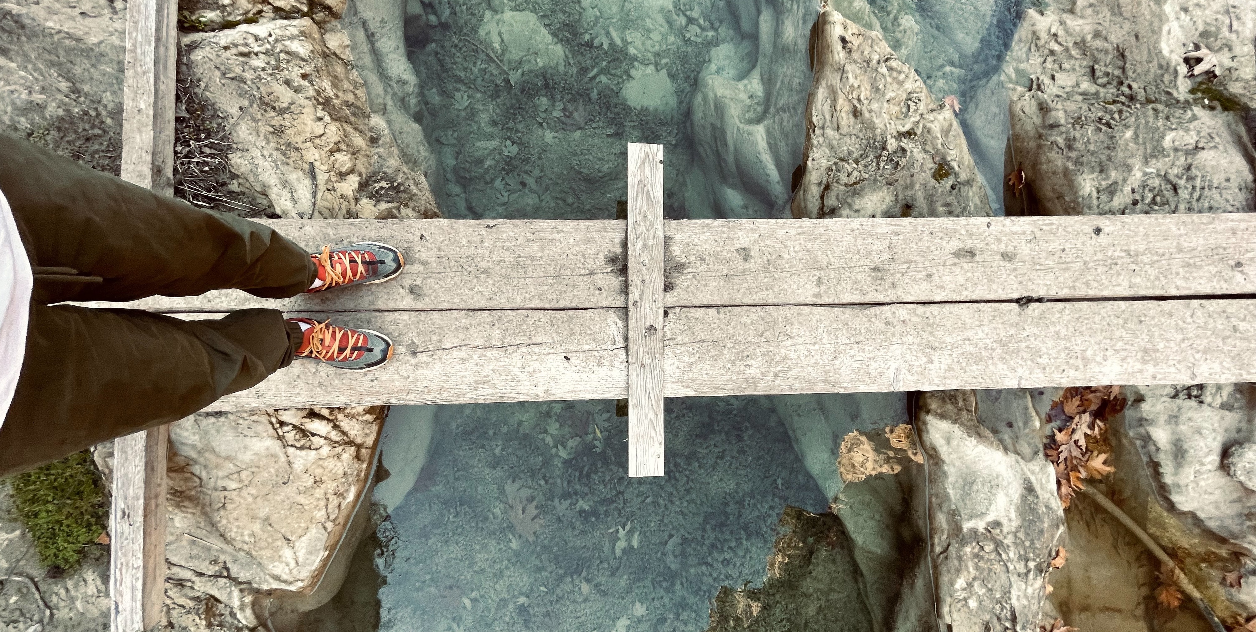 "hiker crossing a small wood-plank bridge across a rocky chasm"