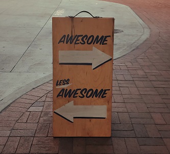 Sign on a pavement with the word "awesome" above an arrow pointing to the right, and the words "less awesome" above an arrow pointing to the left