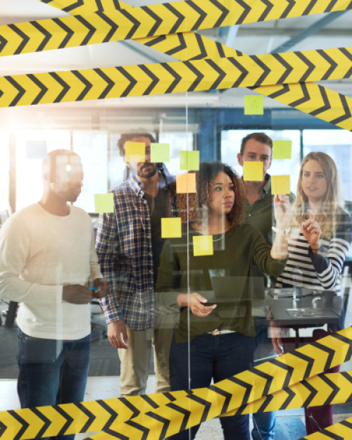 A group of coworkers stands behind a glass wall with sticky notes and yellow caution tape, collaborating in an office.