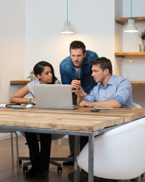 Three coworkers collaborating around a laptop at a table.